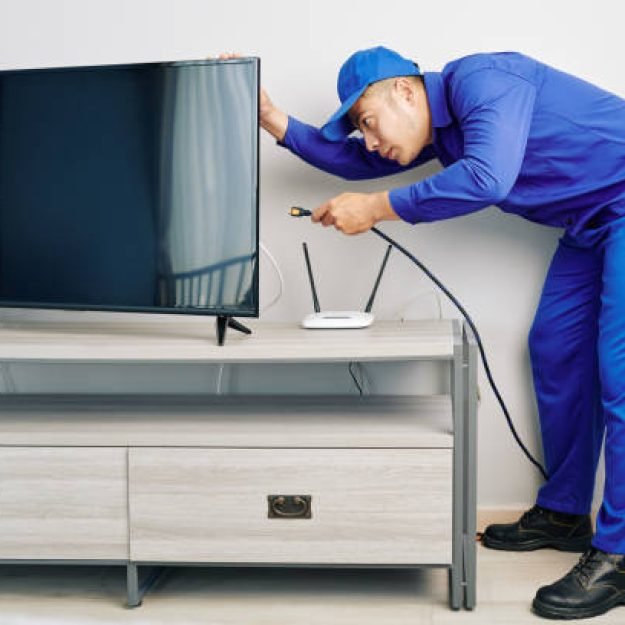 Serious young Vietnamese repairman installing tv set in apartment of customer